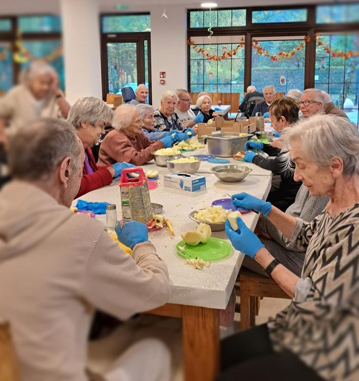 Seniorzy podczas wspólnych zajęć kulinarnych w Domu Seniora Dębowe Wzgórze – obieranie jabłek.